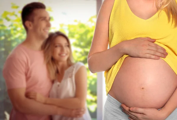 代理出産の概念 若いです妊娠中の女性とぼやけたビューの幸せなカップル屋内 — ストック写真