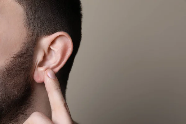 Man Pointing His Ear Grey Background Closeup Space Text — стоковое фото