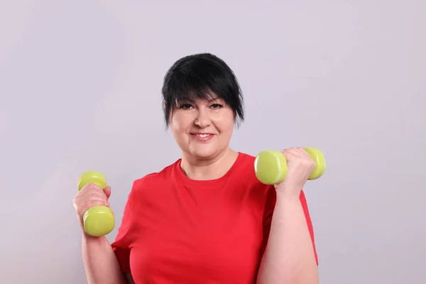 幸せな太りすぎ成熟した女性あります演習とともにダンベル上の灰色の背景 — ストック写真