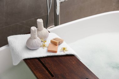 Tahta banyo tepsisi, bitkisel masaj torbaları ve banyo konforları küvette, yakın çekim.