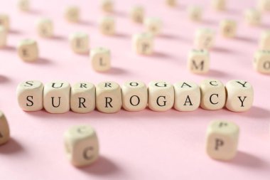 Word Surrogacy made of wooden cubes on pink background, closeup clipart