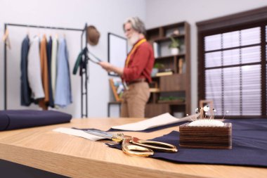 Atölyede çalışan profesyonel terzi, makas ve iğne yastığıyla masaya odaklan. Metin için boşluk