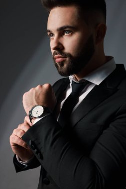 Gri arka planda şık takım elbiseli yakışıklı sakallı adam.