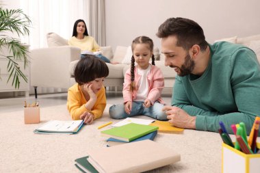 Anne kanepede kitap okurken, baba çocuklarıyla oynuyor.