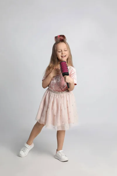 Açık Gri Arka Planda Saç Fırçasıyla Şarkı Söyleyen Sevimli Küçük — Stok fotoğraf