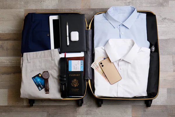 Packed suitcase with business trip stuff on wooden surface, flat lay