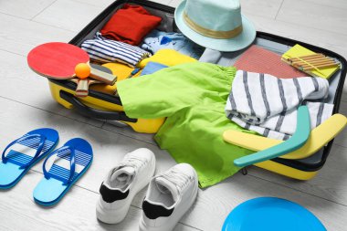 İçinde şık kıyafetler, aksesuarlar, spor malzemeleri ve ayakkabılar olan bavulu açın. Yaz tatili