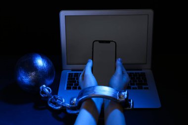 Zincire vurulmuş bir kadın dizüstü bilgisayarın yanında, karanlık arka planda, yakın planda. İnternet bağımlılığı