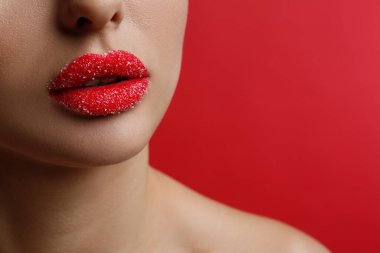 Kırmızı arka planda dudakları şekerle kaplı bir kadının yakın görüntüsü. Metin için boşluk