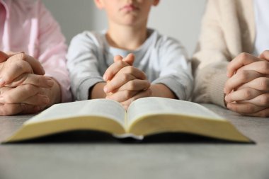Oğlan ve vaftiz ailesi gri masada birlikte dua ediyor. Yakın plan.