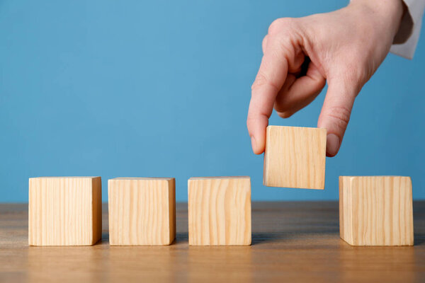 Woman arranging empty cubes in row on wooden table against light blue background, closeup. Space for text