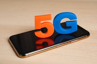 5G teknolojisi, internet konsepti. Ahşap masa üzerinde numarası ve harfi olan akıllı telefon, yakın plan.