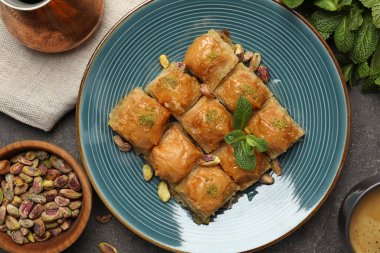 Fıstıklı enfes baklava, fındık, nane ve sıcak kahve gri masada, düz yerde.