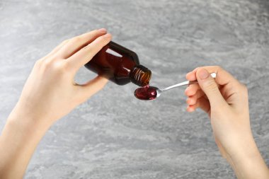 Gri arka planda öksürük şurubunu kaşığa döken kadın, yakın plan.