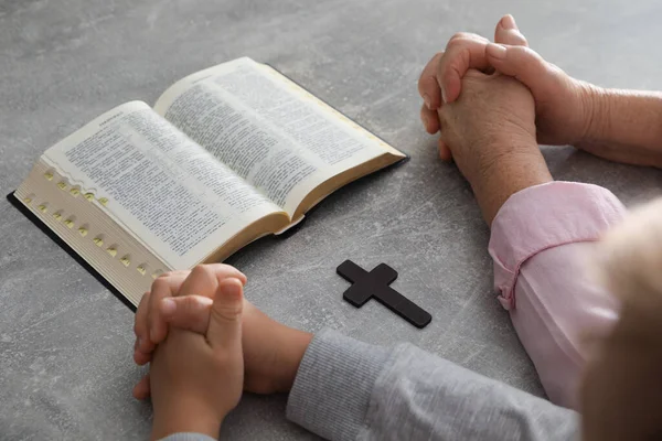 Oğlan ve vaftiz ebeveyni gri masada birlikte dua ediyor. Yakın plan.