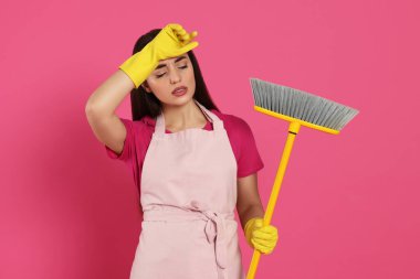 Pembe arka planda süpürgesi olan yorgun genç bir kadın.