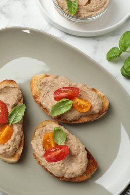 Lezzetli ezmeli ekmek dilimleri, beyaz mermer masada domates ve fesleğen.