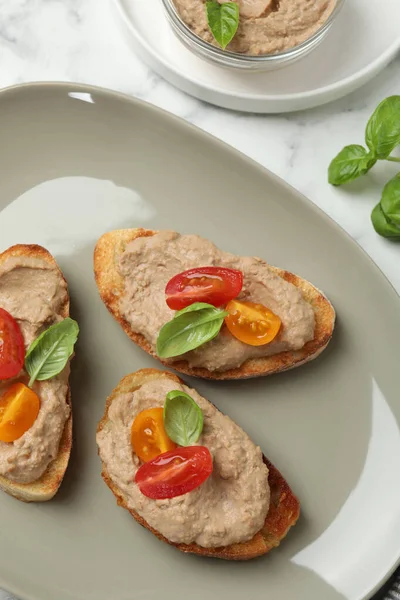 Lezzetli ezmeli ekmek dilimleri, beyaz mermer masada domates ve fesleğen.