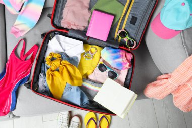 Open suitcase with stylish clothes and accessories on grey sofa, top view. Summer vacation