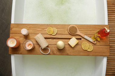 Ahşap banyo tepsisi, mumlar ve banyo konforları küvette, üst manzara.