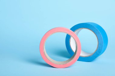 Two bright rolls of adhesive tape on light blue background