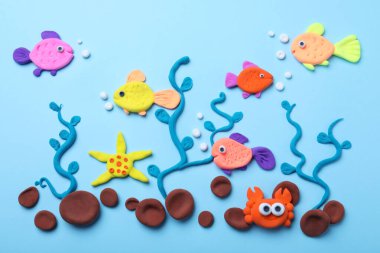 Colorful fish, water plants and stones made with play dough on light blue background, flat lay