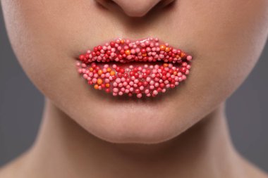 Güzel dudakları olan genç bir kadın. Gri arka planda şekerleme serpiştiriyor. Yakın plan.