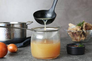 Lezzetli kemik suyunu gri masadaki cam kavanoza koyuyor.