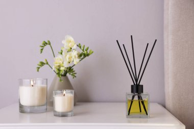 Aromatik kamış oda spreyi, frezya çiçekleri ve beyaz komodindeki mumlar.