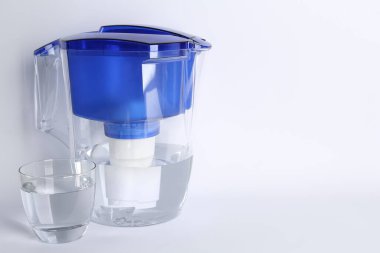 Filter jug and glass with purified water on white background. Space for text