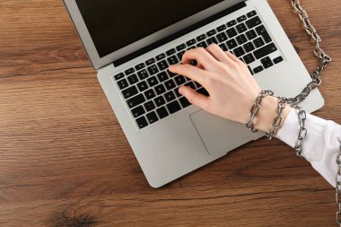 Elleri zincirli bir kadın, ahşap masada dizüstü bilgisayarda yazı yazıyor. İnternet bağımlılığı