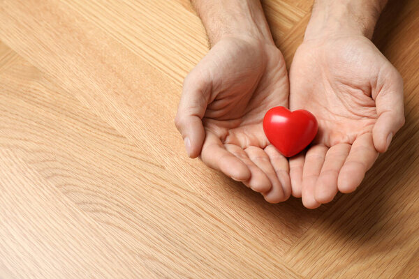 Человек, держащий в руках красное сердце за деревянным столом, крупным планом. Пространство для текста