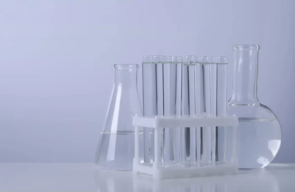 不同的实验室玻璃器皿 有透明的液体放在桌子上 背景明亮 案文的篇幅 — 图库照片
