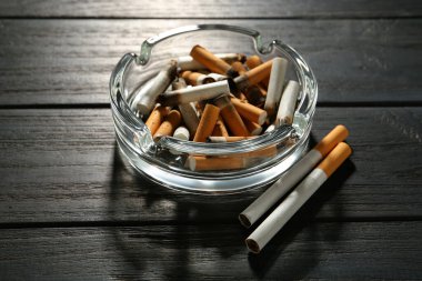 Glass ashtray with cigarette stubs on black wooden table clipart