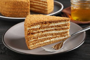 Siyah ahşap masada servis edilen lezzetli katmanlı ballı kek dilimi.