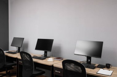 Ofisin içini aç. Açık gri duvarın yanında bilgisayarları olan modern işyerleri