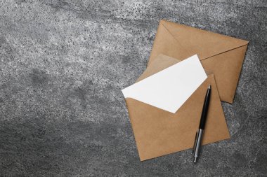 Envelopes with blank paper card and pen on grey table, flat lay. Space for text