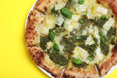 Sarı arka planda pesto, peynir ve fesleğen soslu lezzetli pizza.