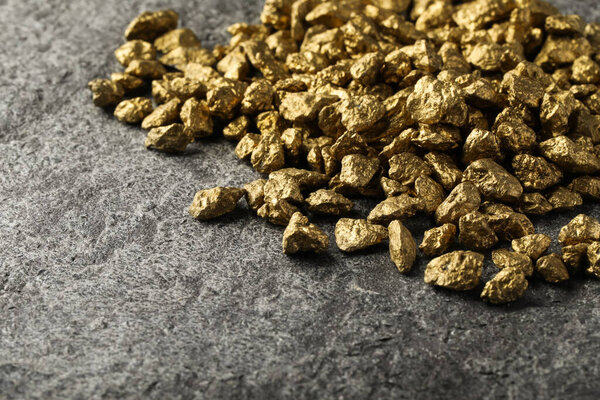 Pile of gold nuggets on grey table, space for text