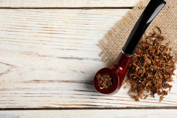 Smoking pipe, dry tobacco and sackcloth on white wooden table, top view. Space for text