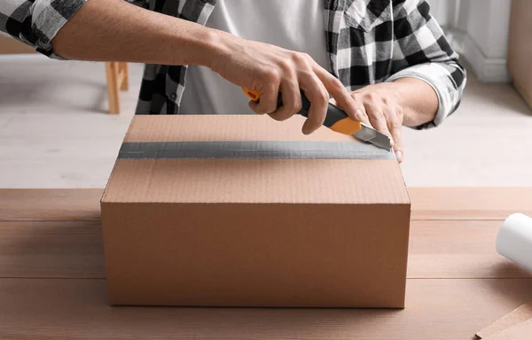 Man Använder Verktygskniv För Att Öppna Paket Vid Träbord Närbild — Stockfoto