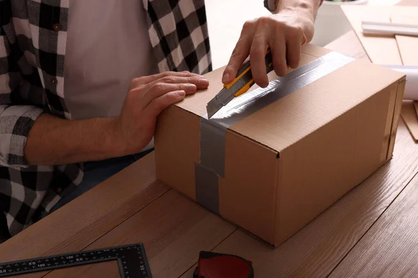 Man Använder Verktygskniv För Att Öppna Paket Vid Träbord Närbild — Stockfoto