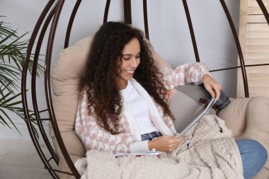 Tabletli Afro-Amerikalı kadın evde yumurta sandalyesinde ders çalışıyor. Uzaklık öğrenimi