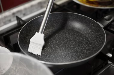 Greasing frying pan on stove in kitchen, closeup