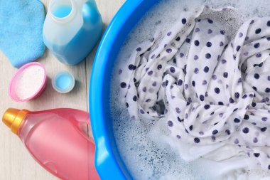 Deterjan şişelerinin yanında köpüklü bir leğen ve yerde toz bezi. El yıkama.