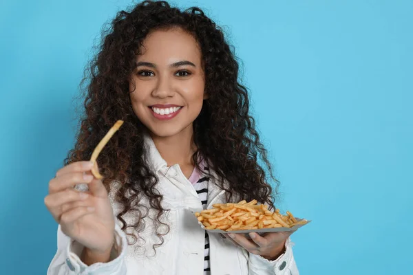 African American woman with French fries on light blue background, space for text