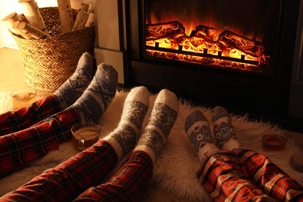 Family in warm socks resting near fireplace at home, closeup of legs