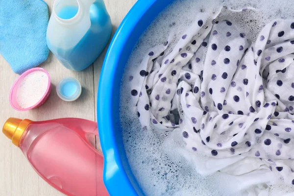 Deterjan şişelerinin yanında köpüklü bir leğen ve yerde toz bezi. El yıkama.