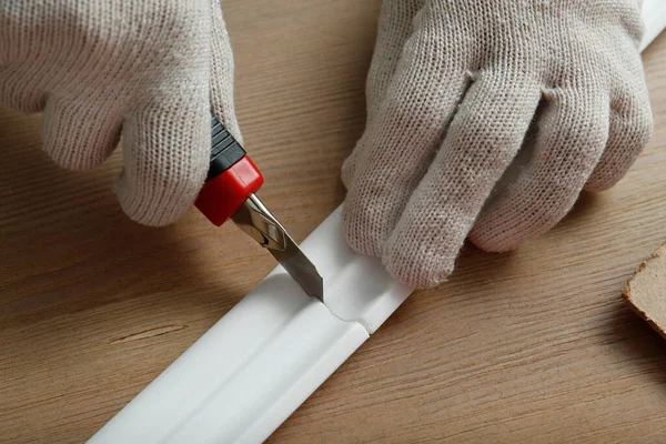 Worker cutting foam crown molding with utility knife at wooden table, closeup