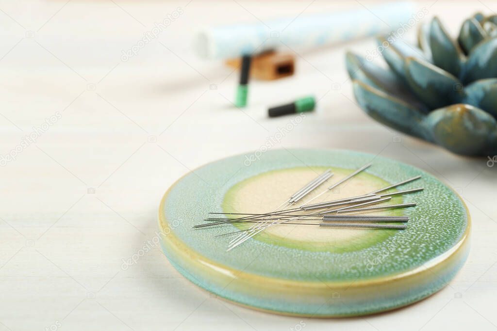 Light green stone coaster with acupuncture needles on white wooden table, closeup. Space for text